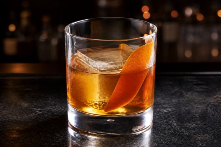 Fancy Free served in a rocks glass over a large ice cube, amber in color, garnished with an orange twist.