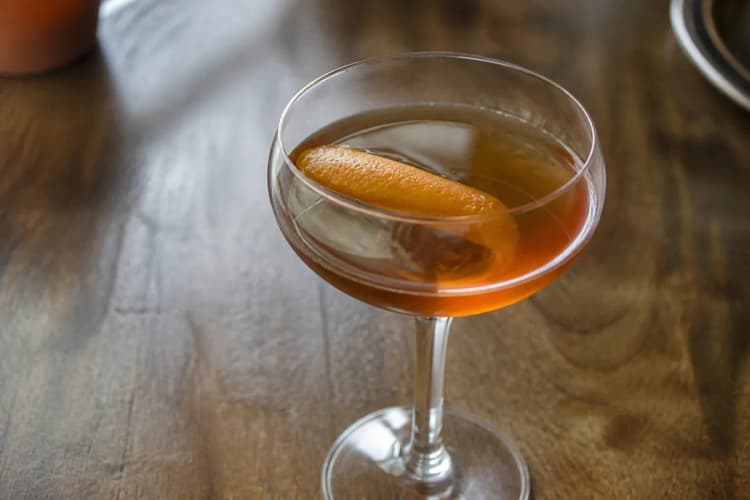 Mezcal Martinez in a coupe, amber, orange peel.
