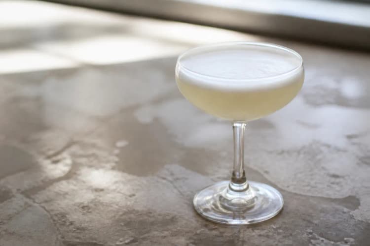 Mezcal Sour in a coupe, pale with soft foam, ungarnished.