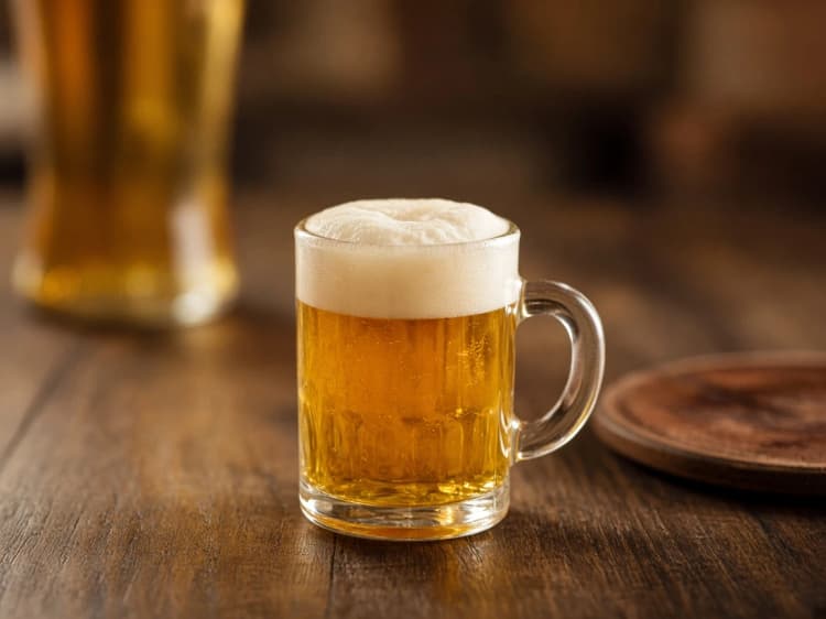 Mini Beer shot of golden Licor 43 with a cream foam head on a warm pub table.