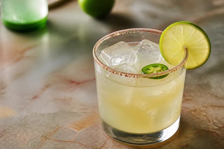 Spicy Margarita in a rocks glass over ice, pale, lime wheel, optional chili salt rim.