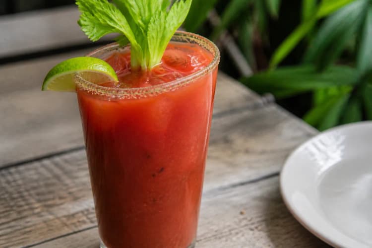 Virgin Mary in a highball over ice, opaque red tomato drink, celery stalk and lime.