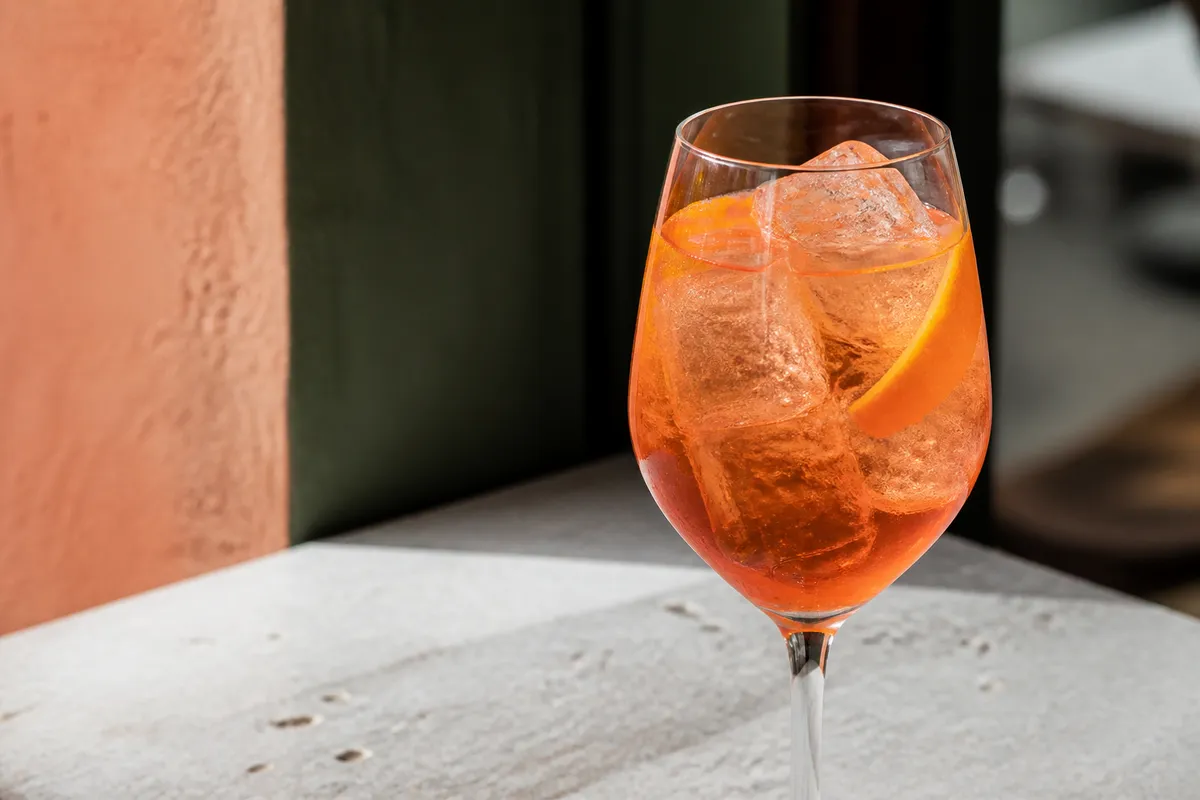 Agave Spritz in a wine glass over ice, orange-pink, orange peel.