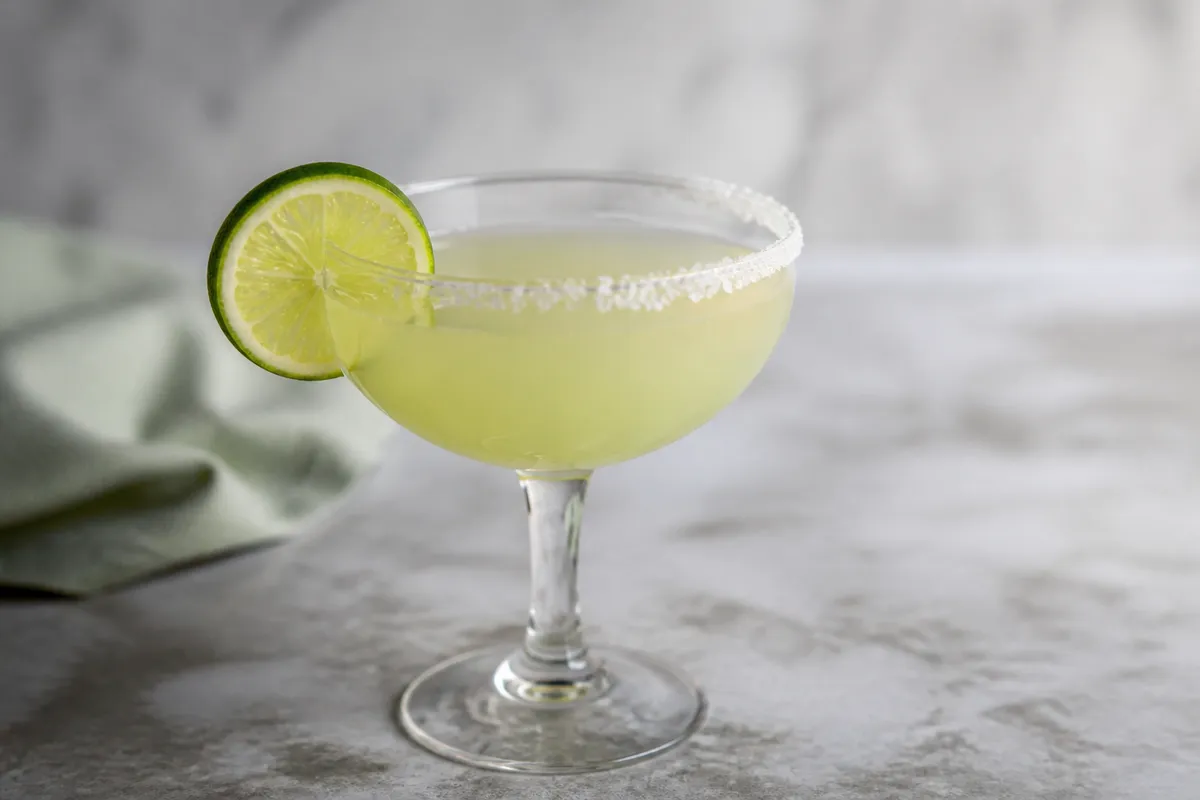 Blanco Margarita in a coupe, pale green, optional salt rim, lime wheel.