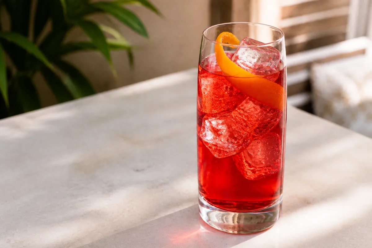 Campari Soda in a highball over ice, bright red, orange peel.