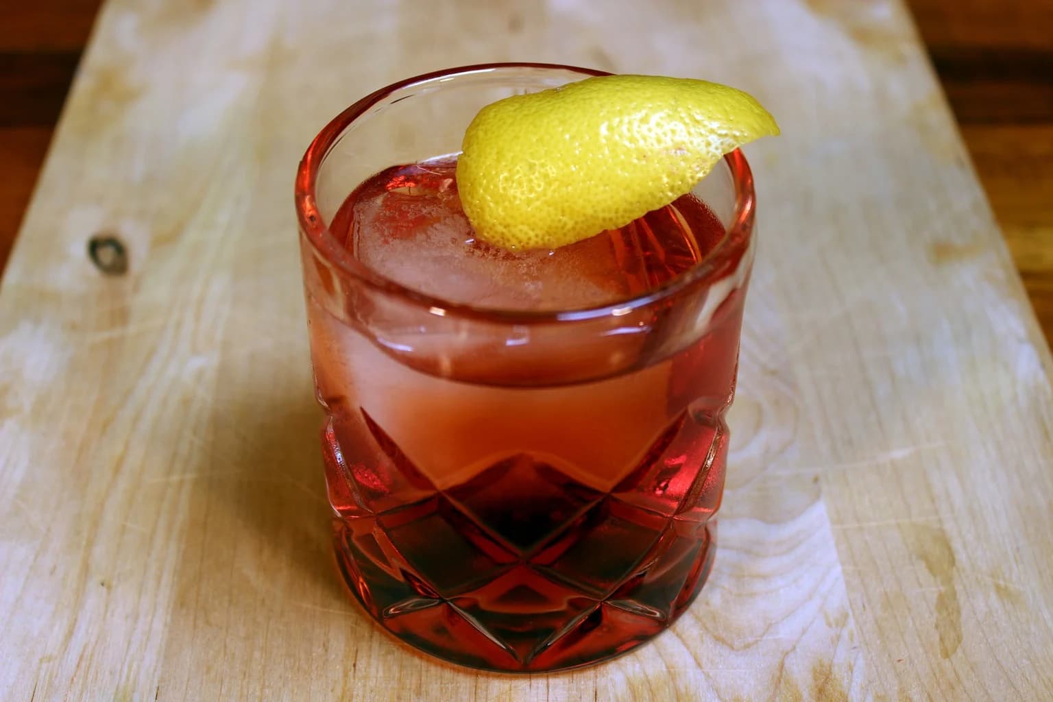 A Negroni in a rocks glass with a large ice cube and orange peel