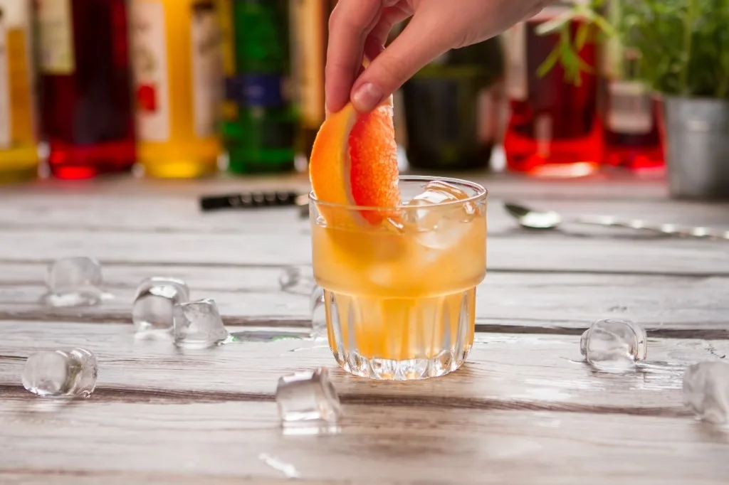 Hand placing a grapefruit wedge garnish on a rocks cocktail