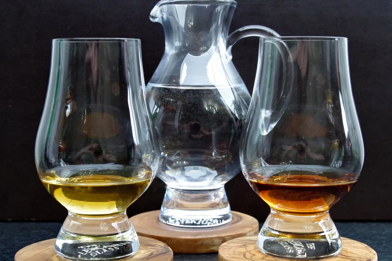 Two Glencairn tasting glasses with different-colored whiskey pours and a water jug between them