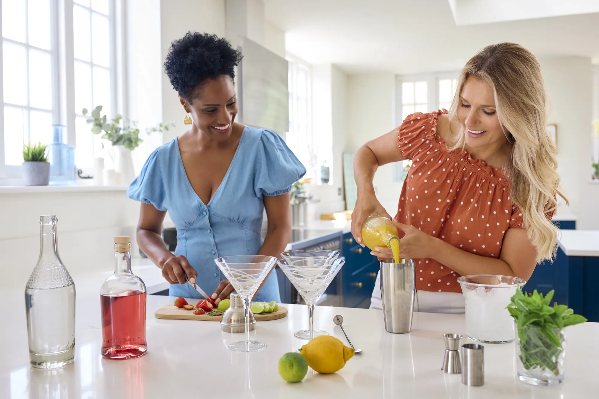 Friends mixing cocktails together in a bright home kitchen