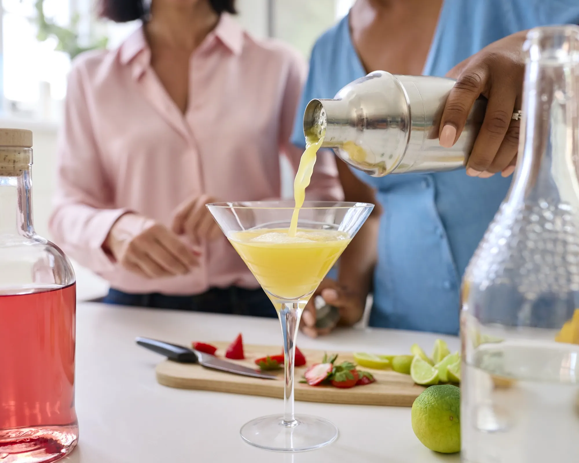 Pouring a shaken cocktail into a coupe at a home kitchen counter
