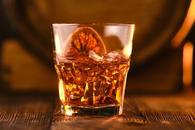 Apple Cider Old Fashioned in a rocks glass over a large ice cube, amber, orange peel garnish.