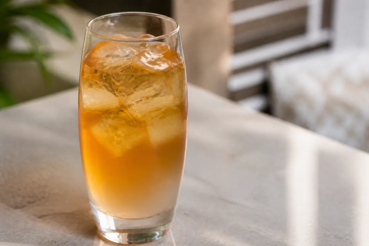 Arnold Palmer in a highball over ice, amber-gold tea-lemonade, lemon wedge optional omit if preferred.