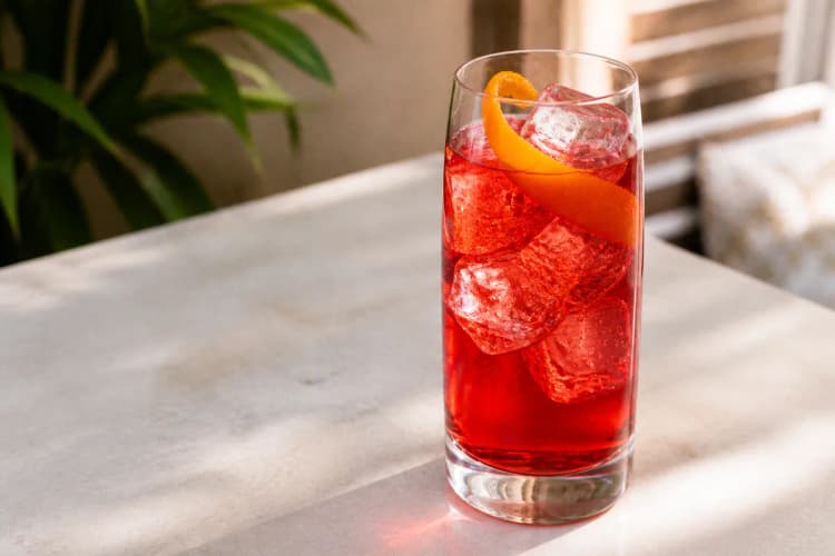 Campari Soda in a highball over ice, bright red, orange peel.