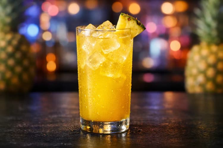 A Caribou Lou in a highball glass with a pineapple wedge.