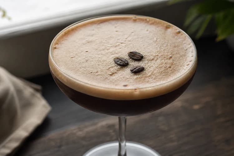 A chilled coupe of Espresso Martini with thick crema and three coffee beans.