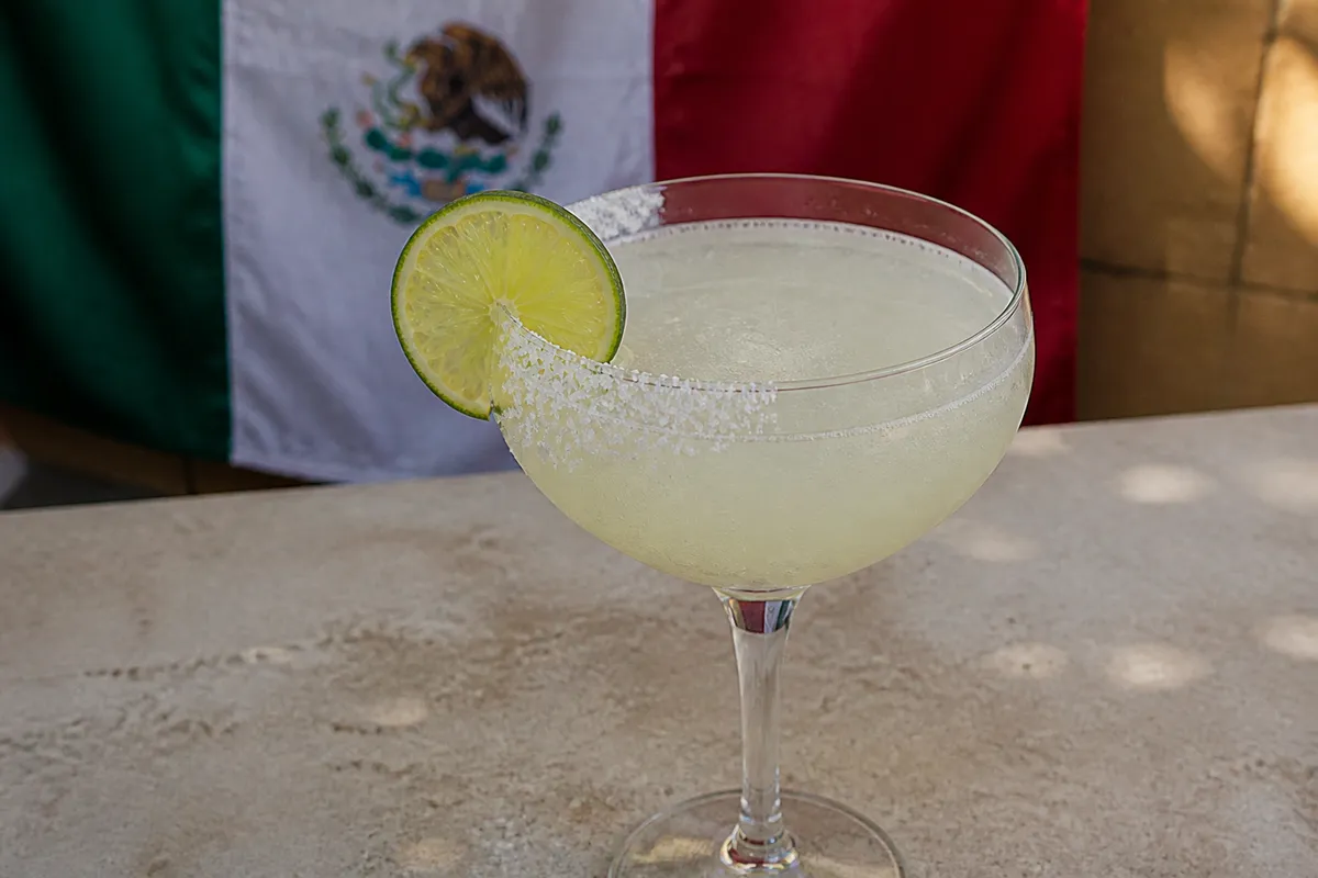 A chilled coupe of Margarita with a half-salt rim and a lime wheel garnish on the edge of the glass.
