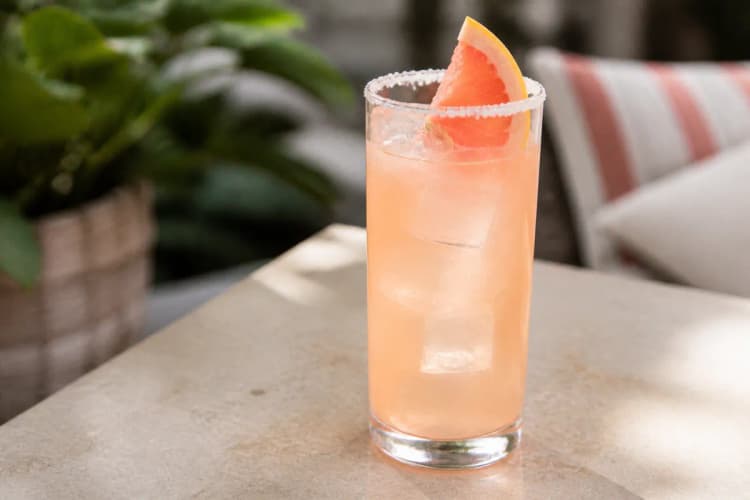 Mezcal Paloma served in a highball glass over ice, pale pink, garnished with grapefruit and optional salt rim.