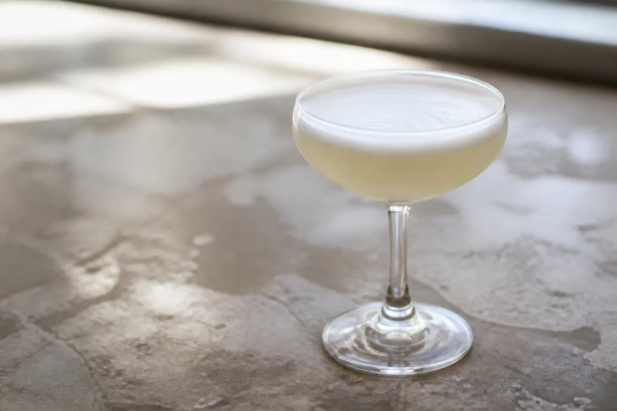 Mezcal Sour in a coupe, pale with soft foam, ungarnished.