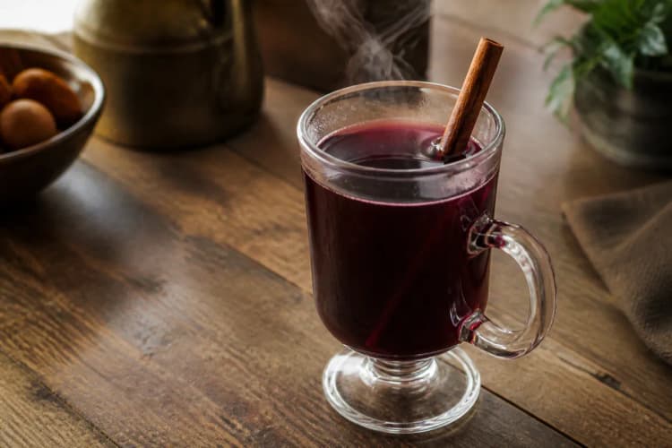 Mulled Wine in a mug, deep red, cinnamon stick and orange peel, light steam.