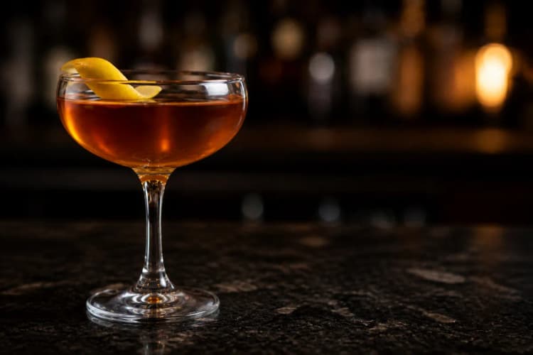 Preakness served in a chilled coupe, amber-brown in color, garnished with a lemon twist.