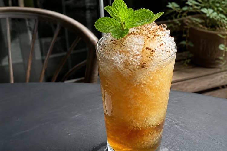 A Queen's Park Swizzle in a tall glass with a red bitters layer and mint bouquet.