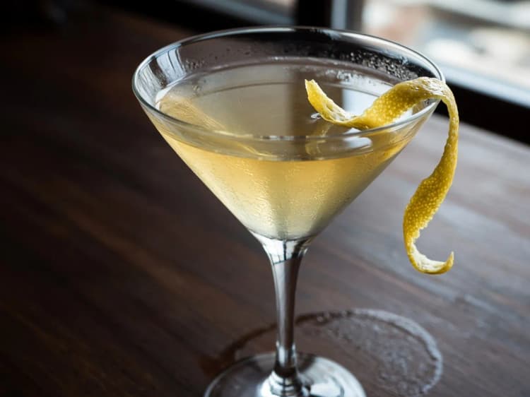 Vesper Cocchi Americano in a V-shaped cocktail glass with a long lemon twist on a dark wood surface.