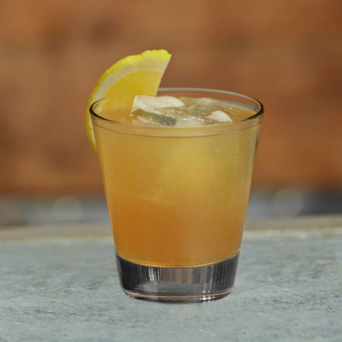A coupe of Tequila Sour with a bright white foam cap and lime zest.