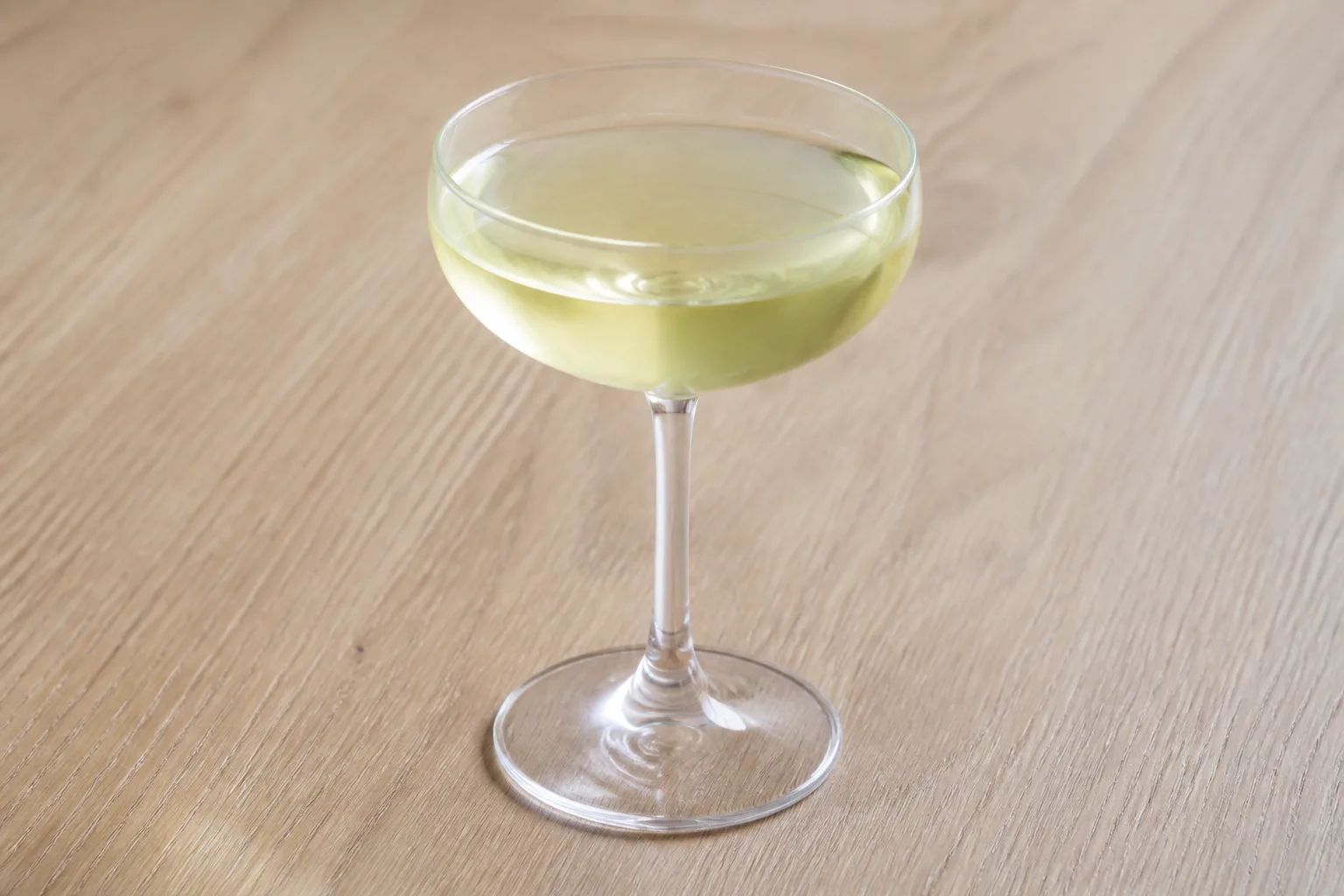 An ungarnished coupe cocktail on a wooden table