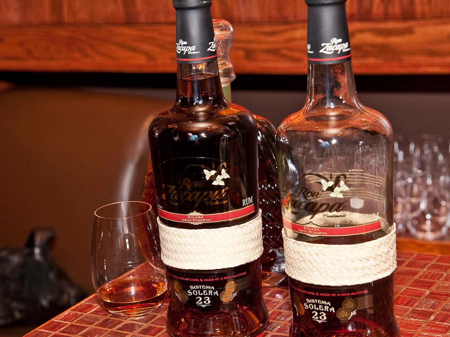 Two dark Zacapa bottles and a tasting glass on a tiled bar