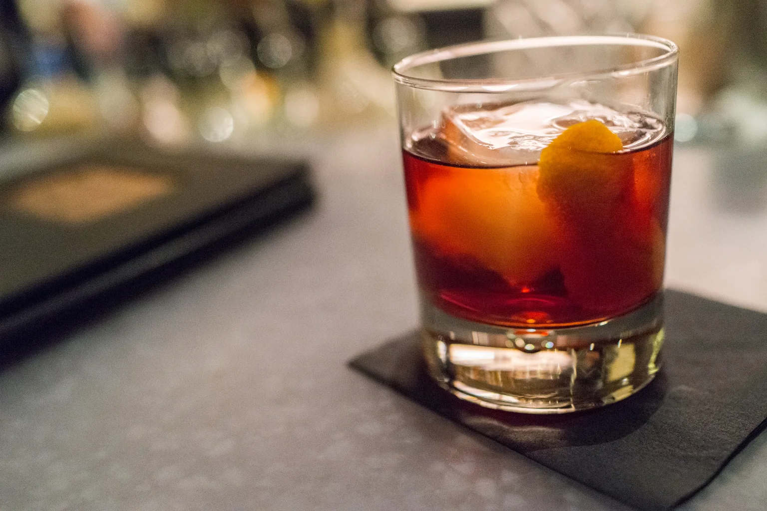 A Boulevardier in a rocks glass with a large ice cube and orange peel