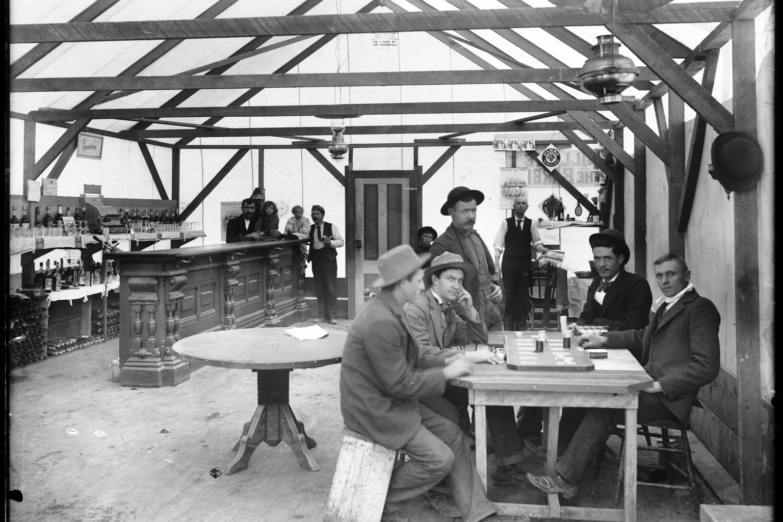 Interior of the Yellow Aster Saloon in Randsburg, California, about 1900 — bottles on the back bar, men at tables