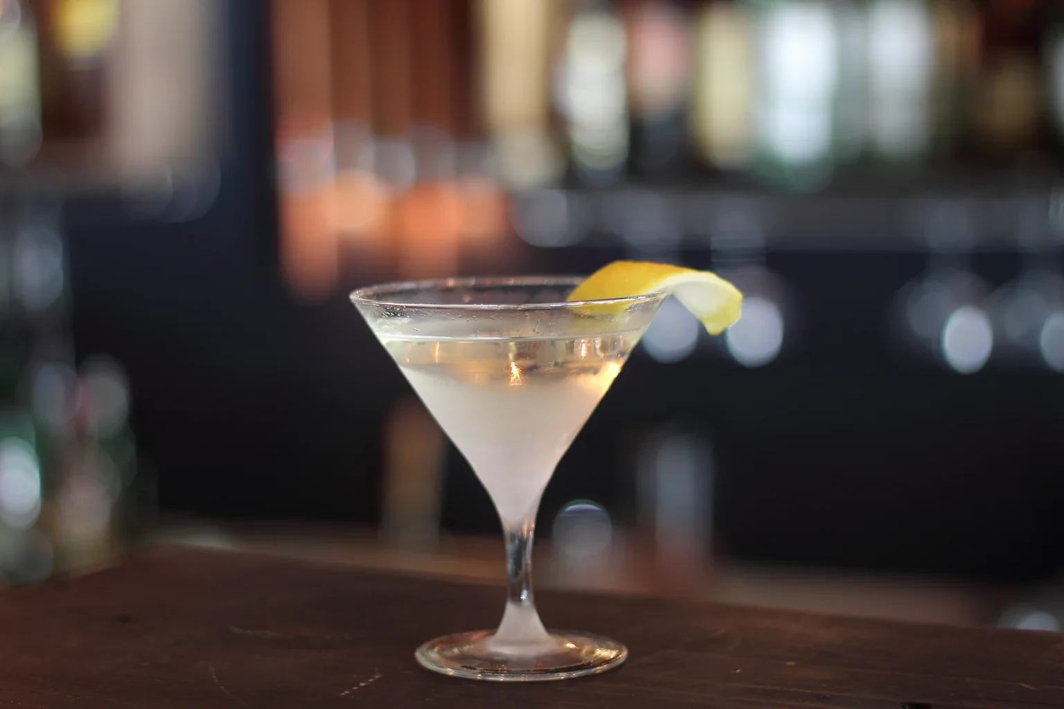 A dry Martini in a V-glass with a lemon twist on a dark bar top